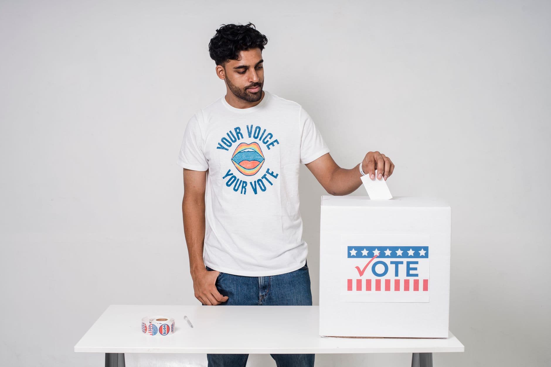 Young man casting a vote into a ballot box on a white background promoting democracy.